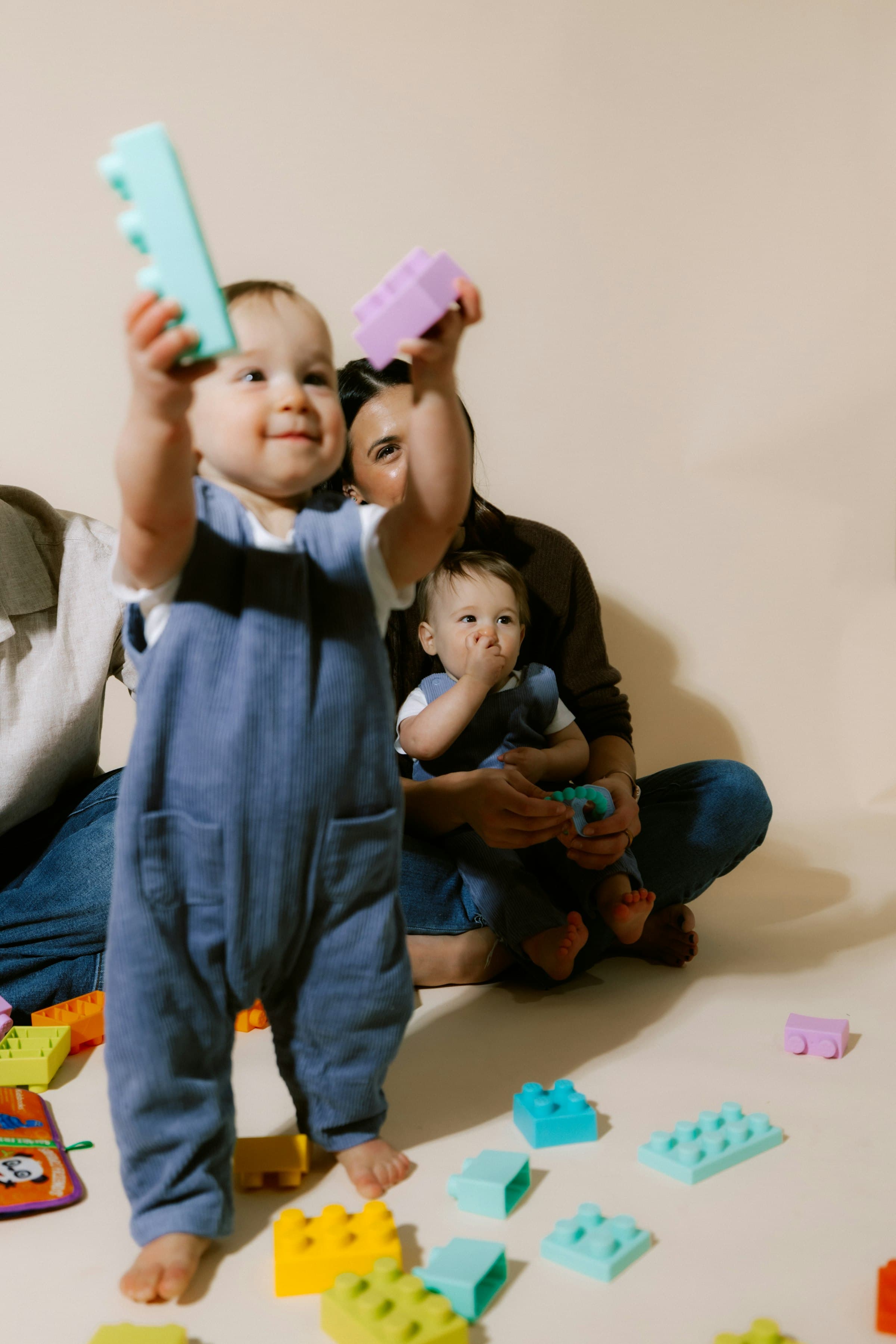 Two adults sitting on the floor with two toddlers, holding up brightly coloured building blocks