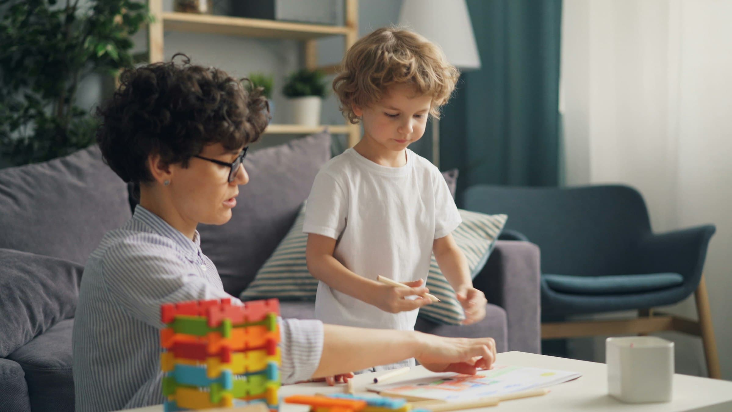 An adult and a young child looking at a picture chart together at a low table, coloured blocks in the foreground